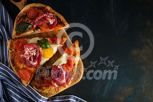 Sliced Homemade tasty pizza with bacon, egg, cheese, tomatoes and basil on dark background. Top view. Sliced Homemade tasty pizza with bacon, egg, cheese, tomatoes and basil on dark background. Top view.