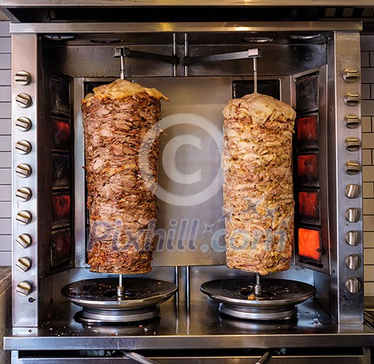 Two rotating skewered chicken and lamb meat grilled in stainless steel grill and ready to serve in a typical Middle Eastern fast food kebab sandwich Two rotating skewered chicken and lamb meat grilled in stainless steel grill and ready to serve in a typical Middle Eastern fast food kebab sandwich