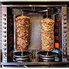 Two rotating skewered chicken and lamb meat grilled in stainless steel grill and ready to serve in a typical Middle Eastern fast food kebab sandwich