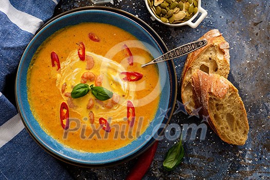 Delicious homemade pumpkin soup with prawns, chili and basil leaves