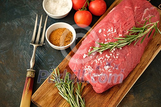 Raw strip loin steak on dark background in rustic style with salt, vegetables and herbs