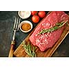 Raw strip loin steak on dark background in rustic style with salt, vegetables and herbs