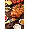 Delicious barbecued ribs seasoned with a spicy basting sauce and served with chopped fresh vegetables on an old rustic wooden chopping board.