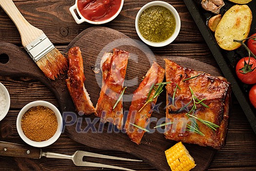 Delicious barbecued ribs seasoned with a spicy basting sauce and served with chopped fresh vegetables on an old rustic wooden chopping board.
