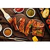 Delicious barbecued ribs seasoned with a spicy basting sauce and served with chopped fresh vegetables on an old rustic wooden chopping board.
