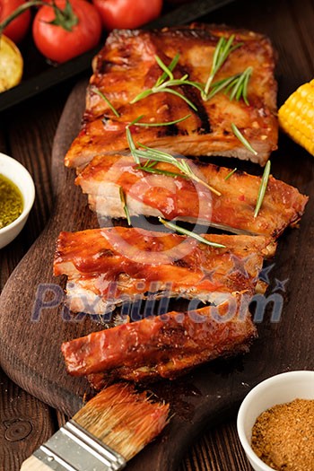 Delicious barbecued ribs seasoned with a spicy basting sauce and served with chopped fresh vegetables on an old rustic wooden chopping board. Delicious barbecued ribs seasoned with a spicy basting sauce and served with chopped fresh vegetables on an old rustic wooden chopping board.