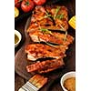 Delicious barbecued ribs seasoned with a spicy basting sauce and served with chopped fresh vegetables on an old rustic wooden chopping board.