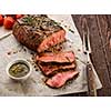 Sliced Roast beef on white paper on wooden table with grilled vegetables 