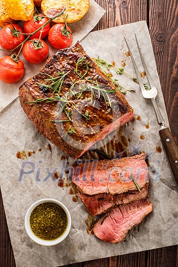 Sliced Roast beef on white paper on wooden table with grilled vegetables Sliced Roast beef on white paper on wooden table with grilled vegetables
