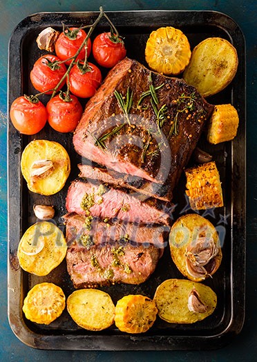 Sliced Roast beef on iron tray with grilled vegetables, top view
