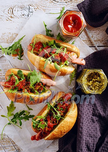 Delicious fresh hot dogs in homemade buns with arugula and ketchup on a wooden background