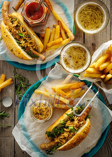 Delicious fresh hot dogs in homemade buns with arugula and ketchup, with beer and French fries on a wooden background