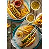 Delicious fresh hot dogs in homemade buns with arugula and ketchup, with beer and French fries on a wooden background