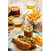 Delicious fresh hot dogs in homemade buns with arugula and ketchup, with beer and French fries on a wooden background