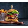 Tasty homemade grilled beef burger with lettuce, cheese and onion served on cutting board on a black wooden table, with copyspace