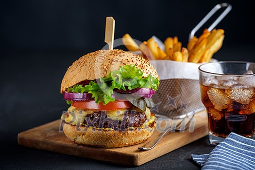 Tasty grilled beef burger with lettuce, cheese and onion served on cutting board on a black wooden table, with copyspace Tasty grilled beef burger with lettuce, cheese and onion served on cutting board on a black wooden table, with copyspace