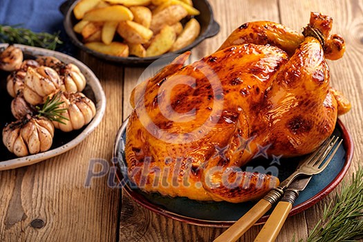 Roasted chicken  in a plate on a wooden table with garlic and potatoes