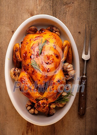 Roasted chicken  with garlic in a white plate on a wooden table. View from above.