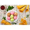 Multicolored balls of cream ice cream on an ice plate, tea and waffle cones on a wooden table.