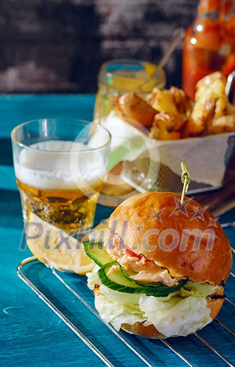 Fishburger with toppings, fries and a glass of beer. Rustic style. Fishburger with toppings, fries and a glass of beer. Rustic style.