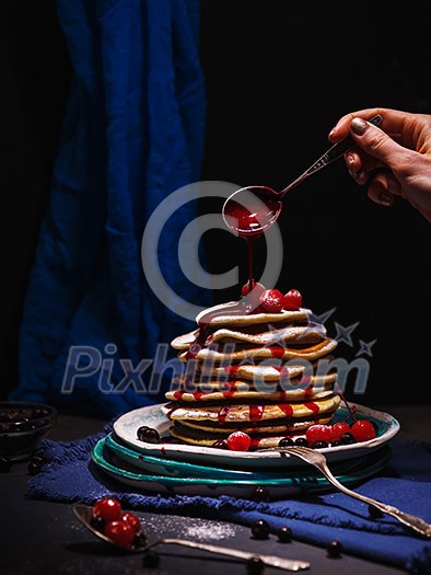 Pancakes with berries and jam on a dark background.