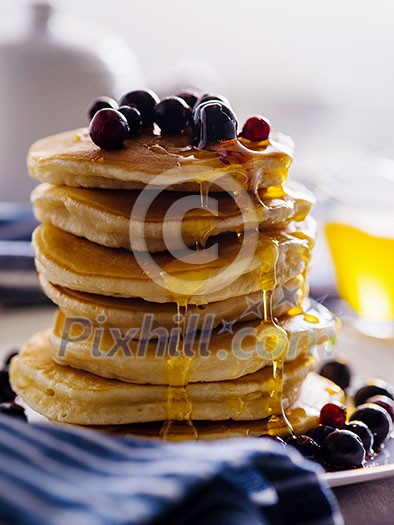 Pancakes with berries and honey on a light background.