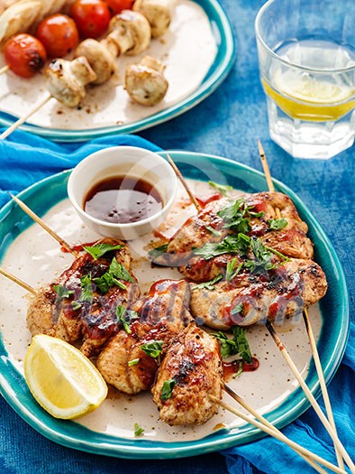 Chicken kebab on skewers with cherry, mushrooms and barbecue sauce on a blue background. 