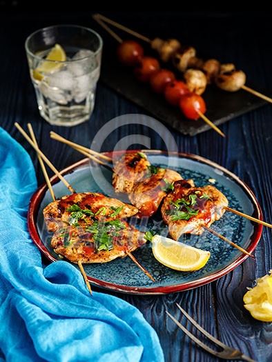 Chicken kebab on skewers with cherry, mushrooms and barbecue sauce on a blue background. 