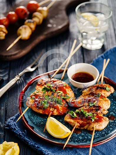 Chicken kebab on skewers with cherry, mushrooms and barbecue sauce on a blue background. 