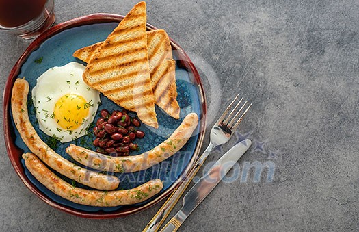 Traditional full English breakfast with fried eggs, sausages and beans on grey background. Top view. Traditional full English breakfast with fried eggs, sausages and beans on grey background. Top view.