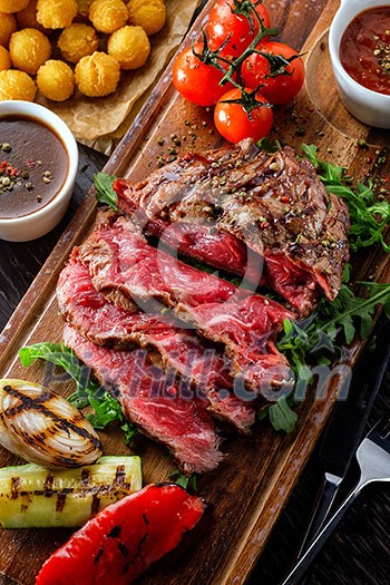 Juicy rare sliced grilled fillet steak served with tomatoes and roast vegetables on an old wooden board. Top view. 