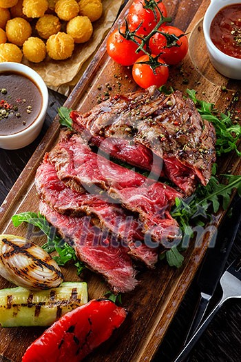 Juicy rare sliced grilled fillet steak served with tomatoes and roast vegetables on an old wooden board. Top view. Juicy rare sliced grilled fillet steak served with tomatoes and roast vegetables on an old wooden board. Top view.