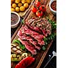 Juicy rare sliced grilled fillet steak served with tomatoes and roast vegetables on an old wooden board. Top view. 
