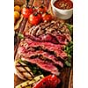 Juicy medium rare sliced grilled fillet steak served with tomatoes and cheese balls on an old wooden board. Top view.