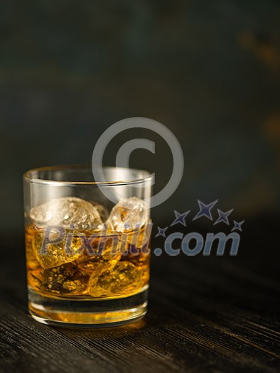 Glass of whiskey with ice on a wooden table. Shallow depth of field