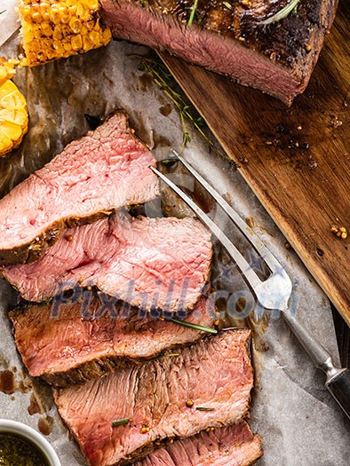 Sliced Roast beef on white paper on wooden table with grilled vegetables Sliced Roast beef on white paper on wooden table with grilled vegetables