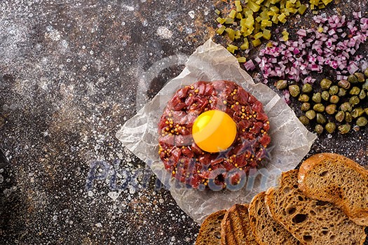 Fresh Beef Tartar is served with yolk, fried bread, pickled cucumbers and capers. Top view