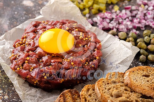 Fresh Beef Tartar is served with yolk, fried bread, pickled cucumbers and capers.