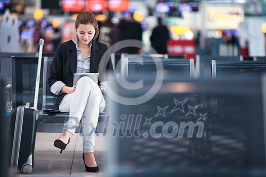 Young female passenger at the airport, using her tablet computer while waiting for her flight (color toned image)