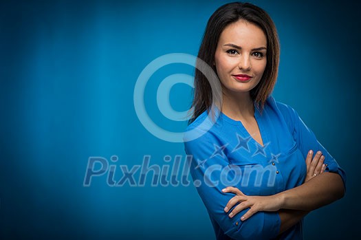 Pretty, young businesswoman with folded arms against blue background