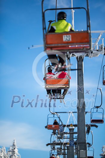 Ski lift with skiers being carried up the hill on a lovely, sunny winter day