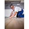 DIY, repair, building and home concept - close up of male hands lying parquet floor board/laminate flooring (shallow DOF; color toned image)