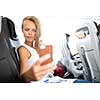 Young happy woman making selfie photo with passport document sitting on the aircraft seat near a window during the flight in the airplane