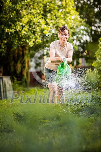 Young woman watering plants and flowers in the garden at summertime. Gardening girl watering flowers with green watering can on a sunny day evening