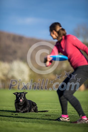 Young woman throwing freisbee to her black dog outdoors (shallow DOF, sharp focus