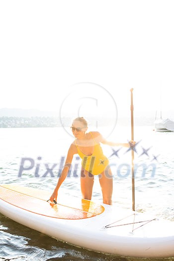 SUP Stand up paddle board concept - Pretty, young woman paddle boarding on a lovely lake in warm late afternoon light SUP Stand up paddle board concept - Pretty, young woman paddle boarding on a lovely lake in warm late afternoon light