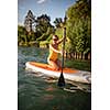 SUP Stand up paddle board concept - Pretty, young woman paddle boarding on a lovely lake in warm late afternoon light