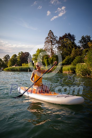 SUP Stand up paddle board concept - Pretty, young woman paddle boarding on a lovely lake in warm late afternoon light SUP Stand up paddle board concept - Pretty, young woman paddle boarding on a lovely lake in warm late afternoon light