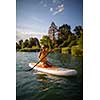 SUP Stand up paddle board concept - Pretty, young woman paddle boarding on a lovely lake in warm late afternoon light