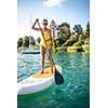 SUP Stand up paddle board concept - Pretty, young woman paddle boarding on a lovely lake in warm late afternoon light